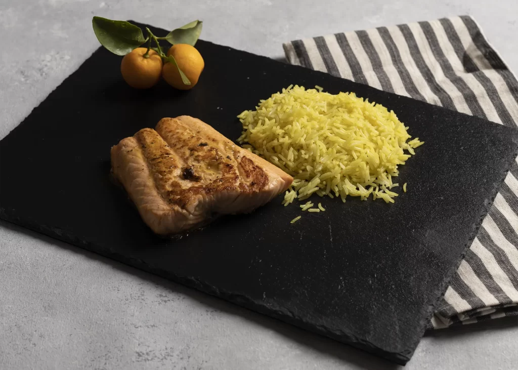 Salmón a la Mandarina con arroz sobre plato negro con mandarinas decorando